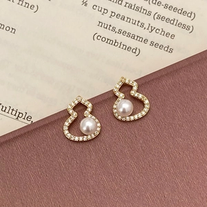 Détails de boucles d'oreilles gourde dorées avec zircons et perles sur des pages de livre