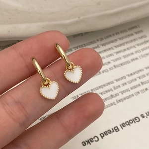 Détail de boucles d'oreilles pendantes dorées avec cœurs blancs et bords perlés chic
