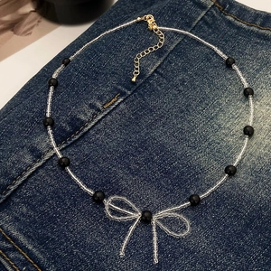 Detail of handmade beaded necklace featuring black beads and a bow pendant with lobster clasp