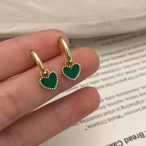 Détail de boucles d'oreilles cœur vert avec bordure perlée dorée dans un cadre chaud