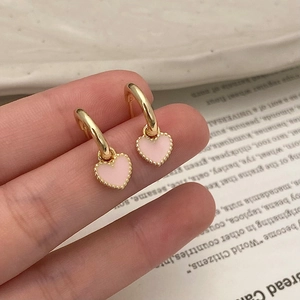 Gros plan de boucles d'oreilles cœur rose avec bords dorés tenues à la main
