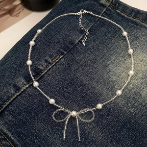 Detail of French style pearl necklace with handcrafted bow pendant on denim background