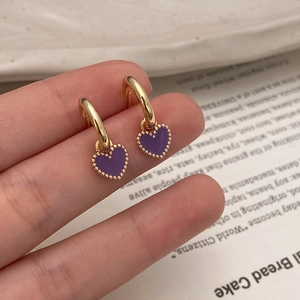 Détail de boucles d'oreilles cœur dorées avec émail violet et petites perles dorées