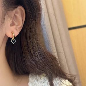 Détail de boucles d'oreilles cœur en or avec émail noir et bord perlé sur mannequin