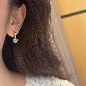 Détail de boucles d'oreilles cœur en or et émail bleu portées par un mannequin