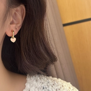 Détail d'une boucle d'oreille cœur rose avec bordure dorée portée par un mannequin