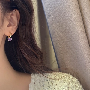Gros plan d'une femme portant des boucles d'oreilles créoles dorées à cœur violet