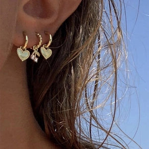 Set de trois boucles d'oreilles dorées avec cœurs et cerises portées par un mannequin