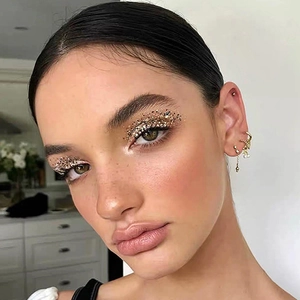 Ensemble de boucles d'oreilles cœur et puces dorées porté par un modèle avec paillettes