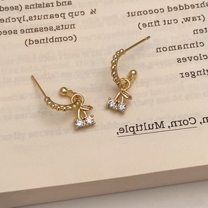 Détail de boucles d'oreilles cerises dorées avec cristaux sur une page de livre