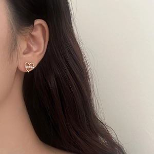 Détail de boucles d'oreilles cœur évidé avec perles dorées portées par une femme