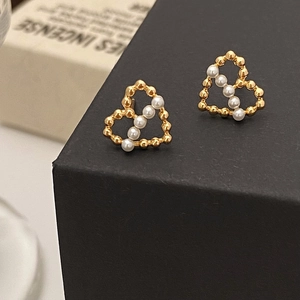 Détail de boucles d'oreilles cœur dorées avec perles blanches sur boîte noire