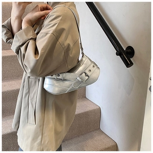 Silver metallic baguette bag with moon-shaped base and eyelet buckle straps in Y2K style