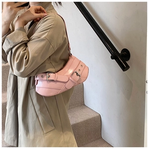 Pink crescent underarm bag with silver buckles and eyelets shown on a tan coat