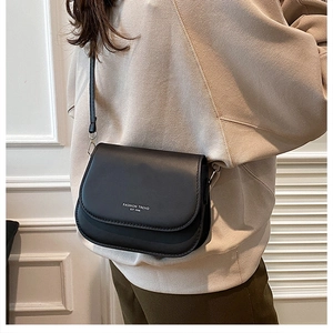Détail d'un sac bandoulière noir avec lettrage blanc porté sur une tenue décontractée