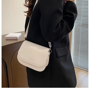 Détail du sac besace en cuir crème avec logo porté sur un modèle en blazer noir