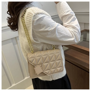 Close-up of beige quilted crossbody bag with gold chain strap worn by a female model