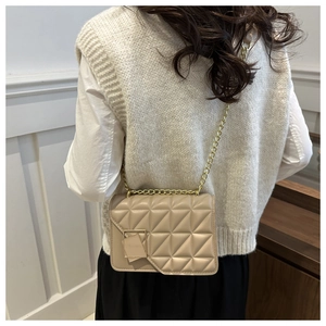 Detail view of beige quilted leather crossbody bag with elegant gold chain strap on model