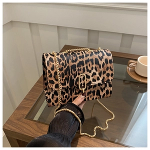 Close-up of leopard print crossbody bag with gold chain strap on a glass table
