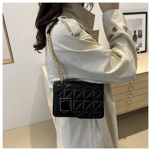 Detail of a black quilted chain bag with gold hardware worn over a beige trench coat