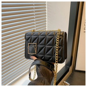 Detail of black quilted leather texture and gold geometric square metal clasp on a handbag