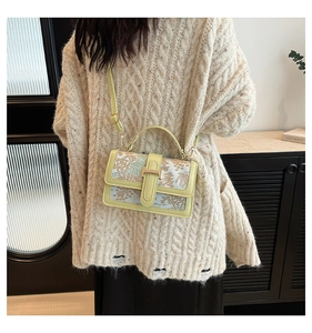 Detail of elegant floral landscape embroidery and golden metal buckle on crossbody bag