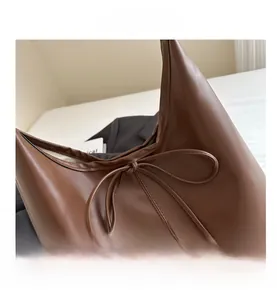 Close-up of brown leather tote bag detail with decorative bow and neat stitching