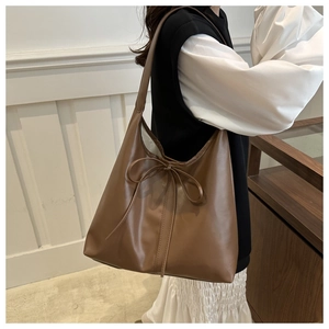 Detail view of large brown tote bag featuring a decorative bow and wide shoulder strap