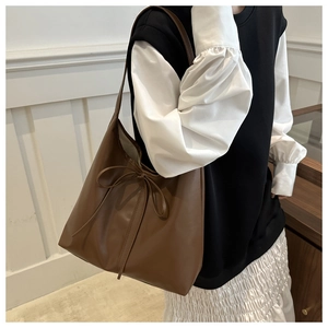 Brown leather tote bag with bow detail shown on shoulder with minimalist outfit