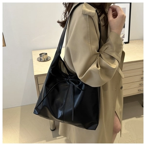 Detail of a large black leather tote bag with a bow tie, worn with a khaki trench coat