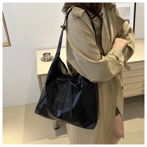 Detail of black large tote bag with bow tie decoration worn with a stylish trench coat
