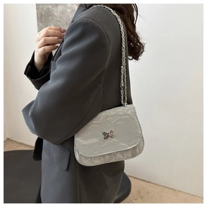 Detail of grey crossbody bag with glossy pleated texture and silver butterfly ornament