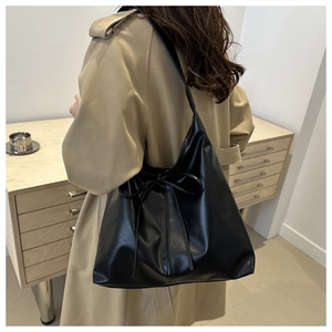 Close-up of black tote bag with bow detail worn by a model in a beige trench coat