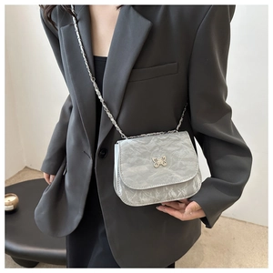 Detail of silver chain strap and butterfly buckle on textured leather crossbody bag