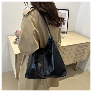 Detailed side view of black pleated tote bag with bow drawstring on model in minimalist room