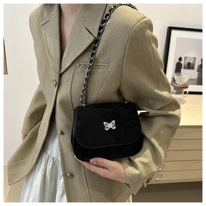 Close-up of black saddle bag with silver butterfly charm and leather chain strap