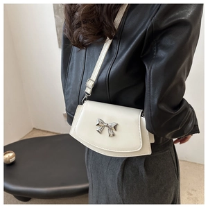 Detail view of a white crossbody bag featuring a silver bow accent on a black leather jacket