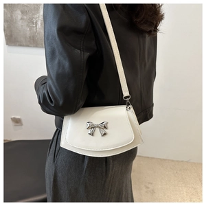 White glossy leather saddle bag with silver bow accent shown on a model
