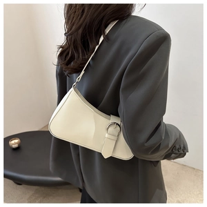 Chic cream crescent underarm bag with glossy finish and metal buckle shown on a shoulder
