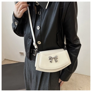 Close-up of white leather saddle bag featuring a decorative silver bow metal clasp