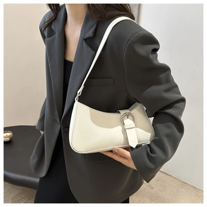 Borsa baguette bianca stile francese indossata a spalla da modella con completo grigio