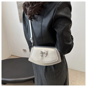 Detail of silver metallic saddle bag featuring a bow accent and polished synthetic leather