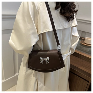Detail of dark brown leather crossbody bag featuring a silver bow buckle on model
