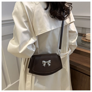 Borsa a tracolla marrone con fiocco d'argento indossata sopra un trench beige chiaro