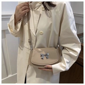 Borsa a tracolla beige con fiocco argentato indossata su un trench alla moda
