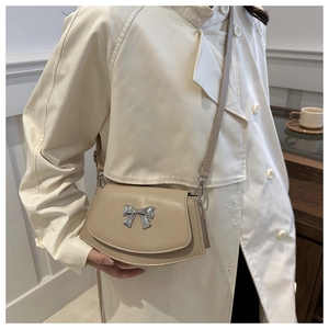 Detail view of a beige saddle bag featuring a decorative silver metal bow on the front