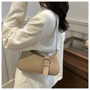 Detail of a beige half-moon underarm bag with a metal buckle worn by a model in a room