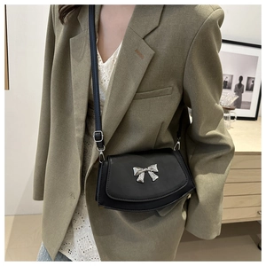 Detail of black leather saddle bag with silver bow accent on olive green blazer outfit