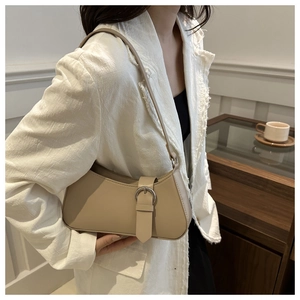 Dettaglio della borsa sottobraccio in pelle kaki con fibbia argento su abito beige