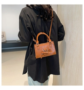 Brown crossbody bag featuring a heart-shaped cutout with a bow knot detail on model